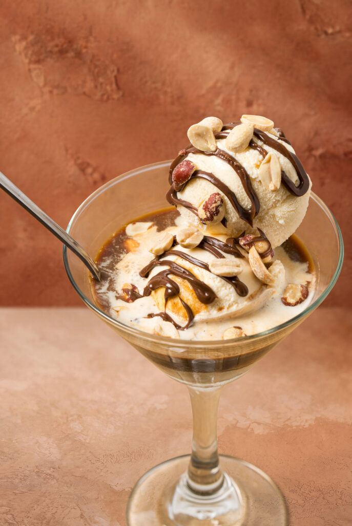 Primer plano de una bola de helado cubierta de salsa de chocolate y maní, sumergida en café dentro de una copa martini.