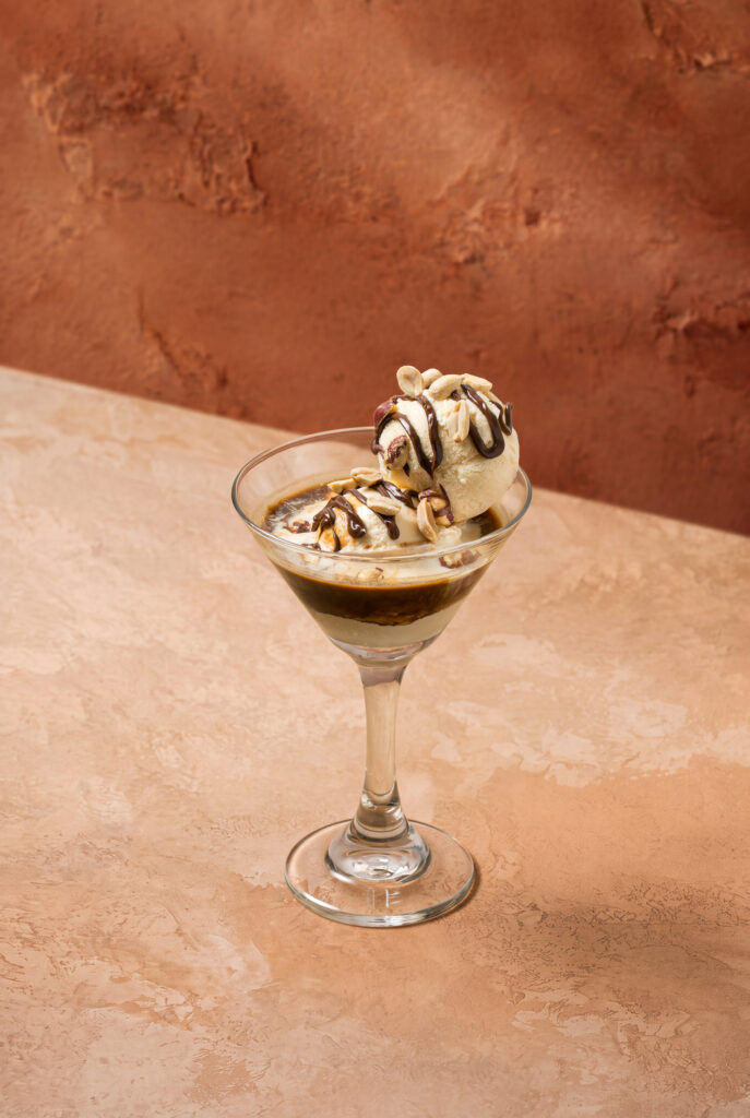 Vista superior de un affogato martini con dos bolas de helado bañadas en café y decoradas con maní y chocolate.