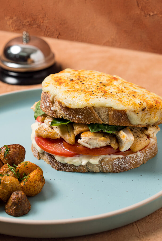 Primer plano de un sandwich de pan tostado con pollo, tomate y capa de queso gratinado burbujeante.
