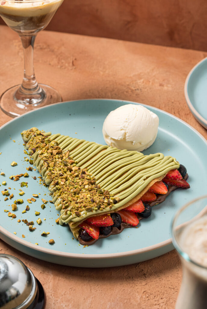 Crepa cubierta de crema de pistacho y pistacho picado, rellena de fresas y arándanos con chocolate, junto a un affogato martini.