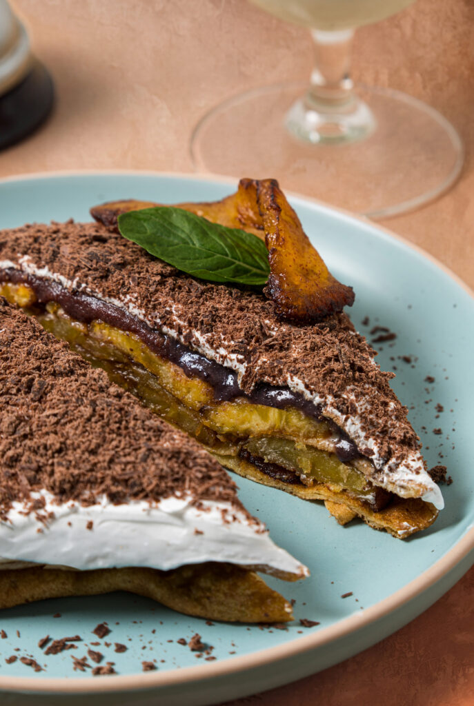 Corte transversal de una crepa rellena de plátano, salsa de chocolate y crema batida, decorada con hoja de menta.