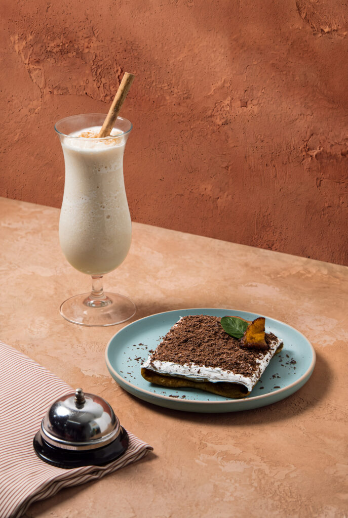 Copa de smoothie de horchata con rajita de canela junto a una crepa de rellenito cubierta de chocolate rallado.