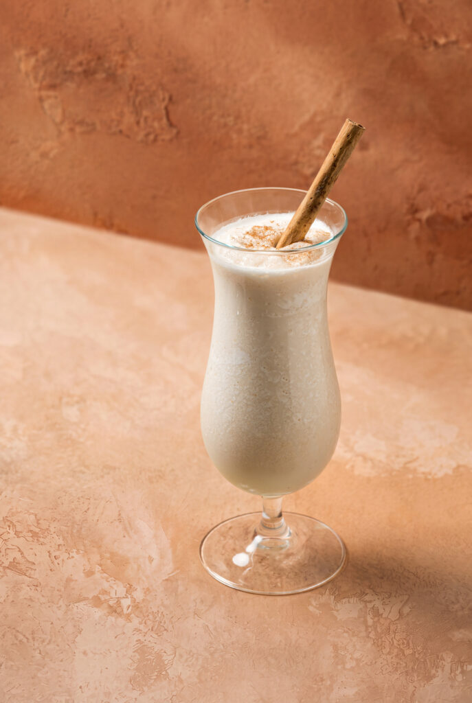 Copa de smoothie de horchata espolvoreada con canela y una rajita de canela como agitador.